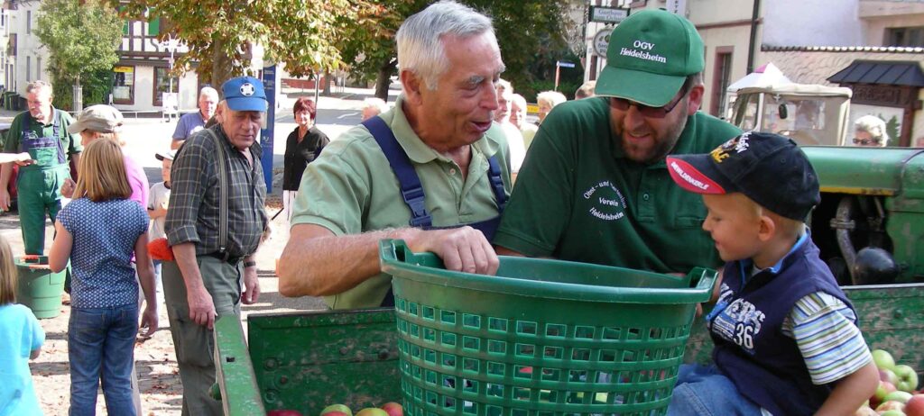 Vereinsmitglieder in Vereinskleidung mit einem Korb Äpfel, daneben ein Junge